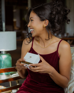 Gift card held in hand; woman in burgundy dress with gold jewelry