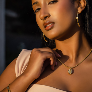 Gold-plated hoop earrings with small textured oval charms on ear